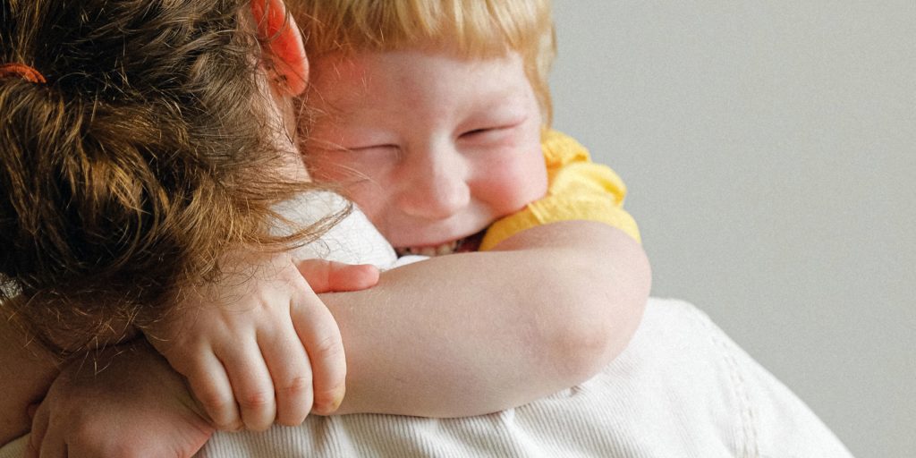 Reunification Month. Preschool age boy smiling and hugging his mom, who is holding him.
