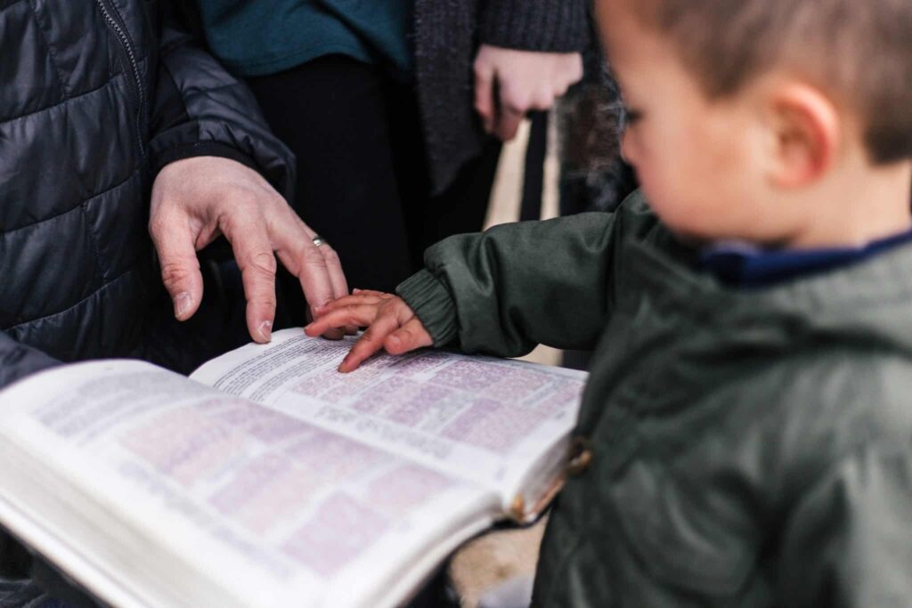 How caring for the widows and orphans impacts your church. Little boy holding open Bible with his parent on the other side.