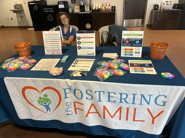 Volunteer sitting at a Fostering the Family table with informational print outs for people to take with them.