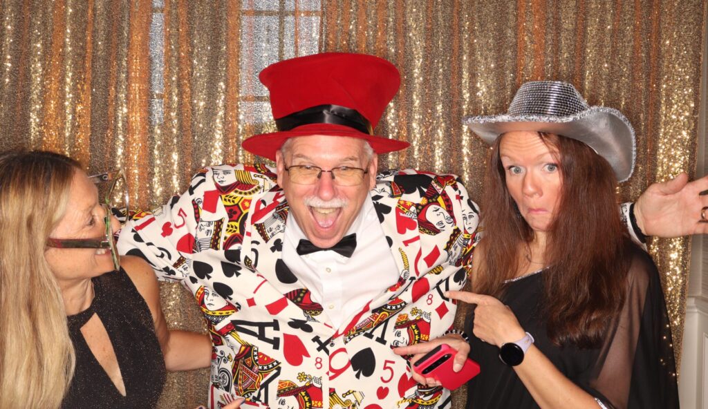 Scott's Story: Scott Bowser in a card deck printed suit jacket and red top hat making a silly face with two coworkers at the 2025 FTF All in for Foster Care Fundraiser